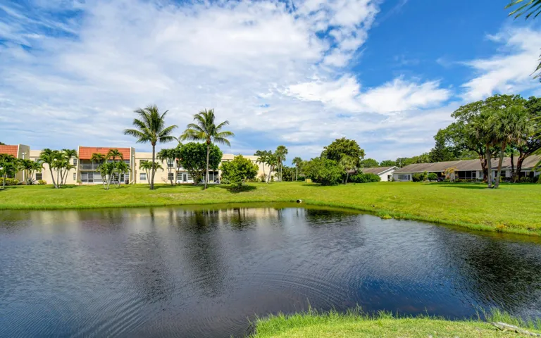 Waterfront property featuring a pond, manicured lawn, and mature trees