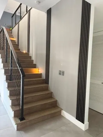 Staircase featuring wood-finish treads, a metal cable railing system, integrated riser lighting, and decorative vertical slat wall detailing