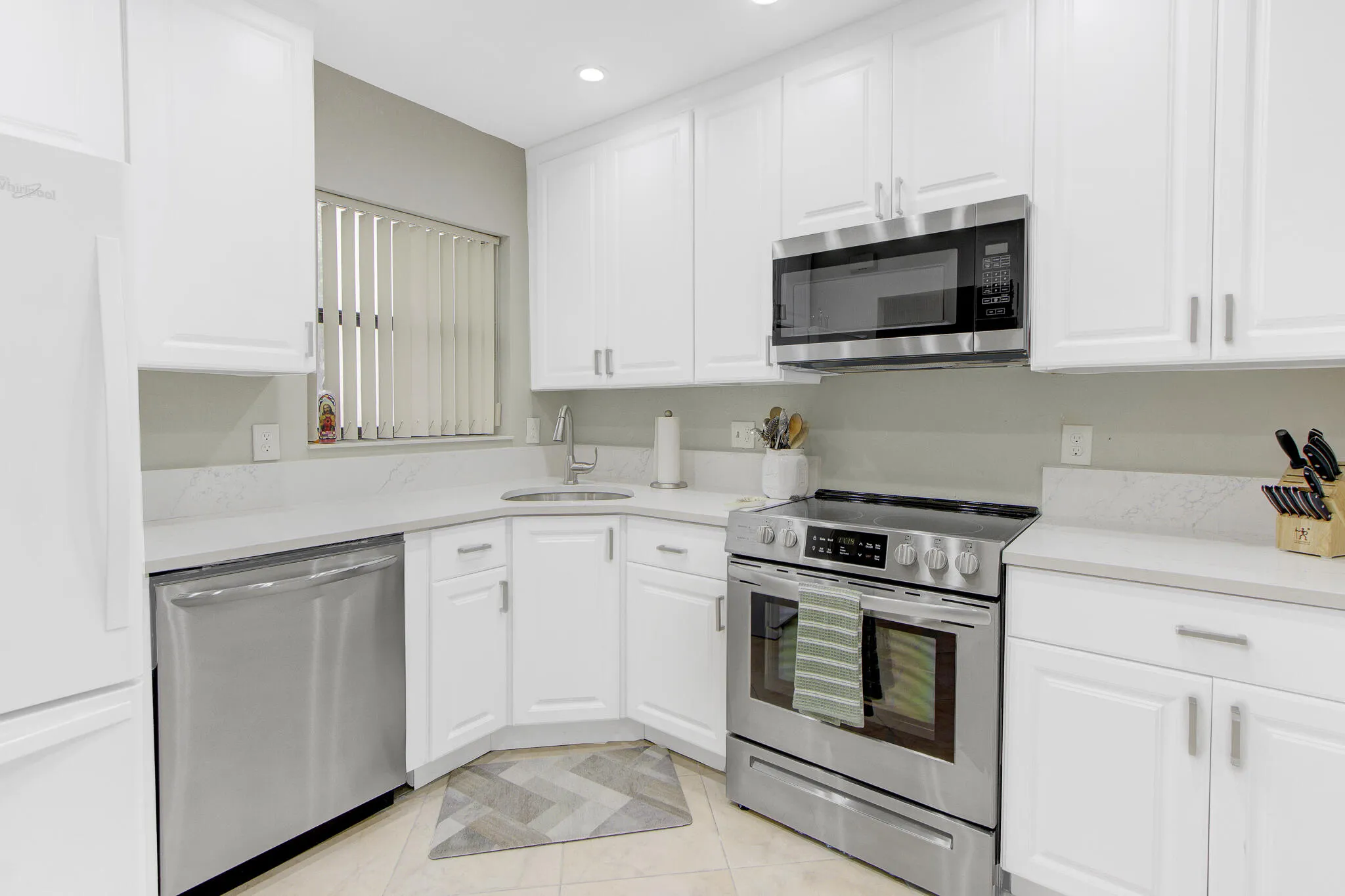 White cabinetry with brushed nickel hardware, stainless steel appliance suite, corner sink, and light-toned countertops