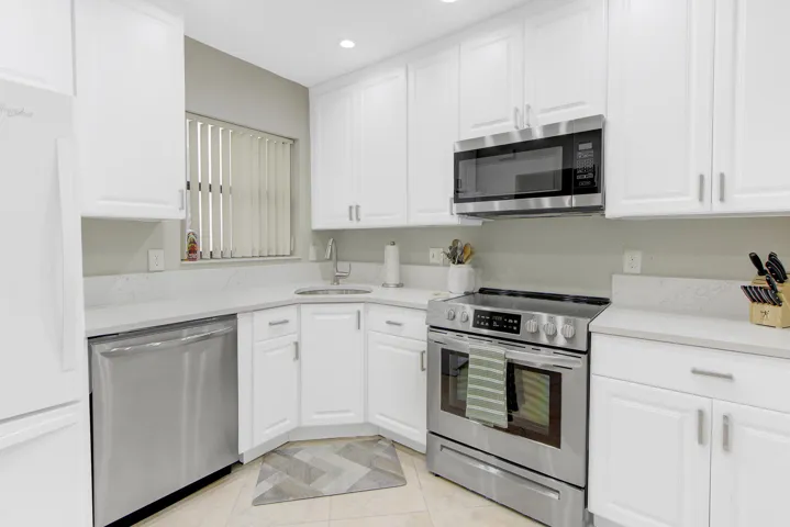 White cabinetry with brushed nickel hardware, stainless steel appliance suite, corner sink, and light-toned countertops