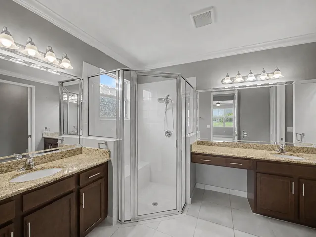 Dual vanity with stone countertops, built-in cabinetry, frameless glass shower enclosure with bench seating, and tile flooring