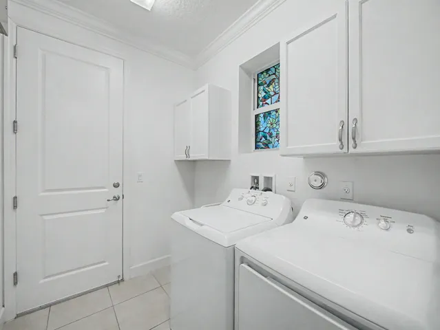 White cabinetry with brushed nickel hardware, stained glass window, crown molding, paneled door, and tile flooring