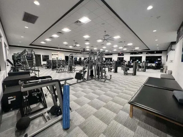 Spacious fitness center featuring varied exercise equipment, patterned carpet flooring, recessed lighting, and ceiling fans