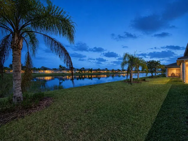 Expansive backyard featuring a manicured lawn, established palm trees, and a lakefront setting
