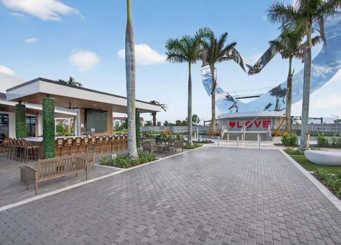 Spacious outdoor bar area with high-top seating, paver walkway, and mature palm trees