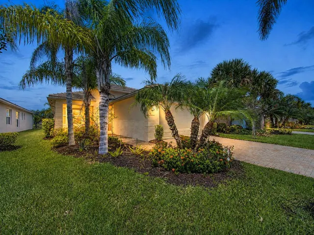 Stucco exterior with a tile roof, mature palm trees, landscaped shrubbery, and a paver driveway