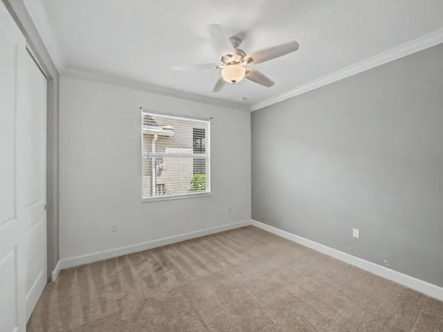 Neutral wall tones, crown molding, ceiling fan with integrated lighting, window with blinds, and carpeted flooring