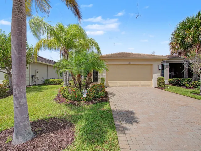 Stucco exterior with a tiled roof, paver driveway, attached garage, and tropical landscaping
