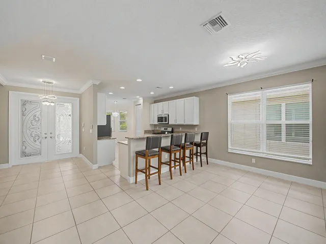 Tile flooring, kitchen island with breakfast bar, white cabinetry, stainless steel appliances, and decorative double entry doors