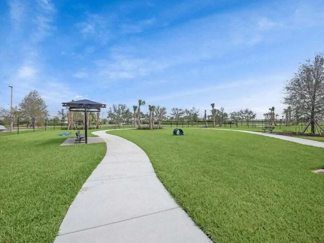 Expansive green space featuring a paved walking path, shade structure, and perimeter fencing