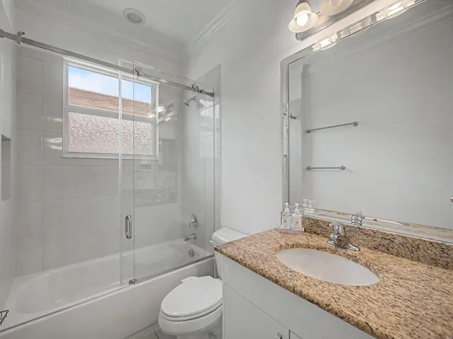 Bathroom featuring a built-in tub with glass sliding doors, tiled shower surround, recessed shower niche, and a vanity with a stone countertop and integrated sink