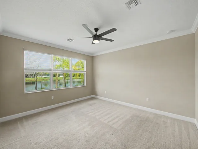 Wall-to-wall carpeting, multiple windows with horizontal blinds, ceiling fan with integrated lighting, and crown molding