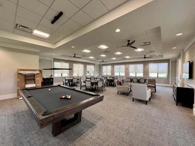 Spacious entertainment area with recessed lighting, ceiling fans, multiple windows, and carpet flooring