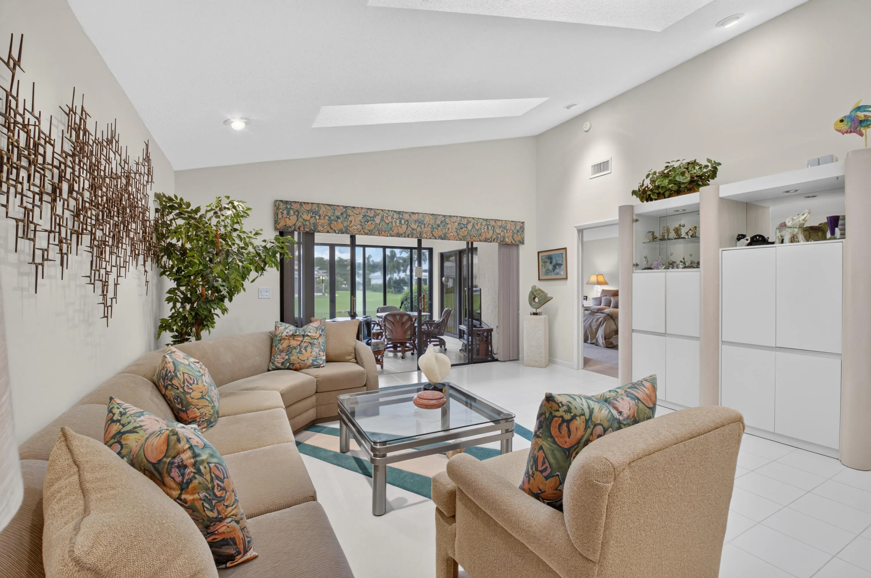 Bright, open living area featuring a curved sectional sofa arrangement, glass-top coffee table, and abundant natural light from multi-panel glass doors