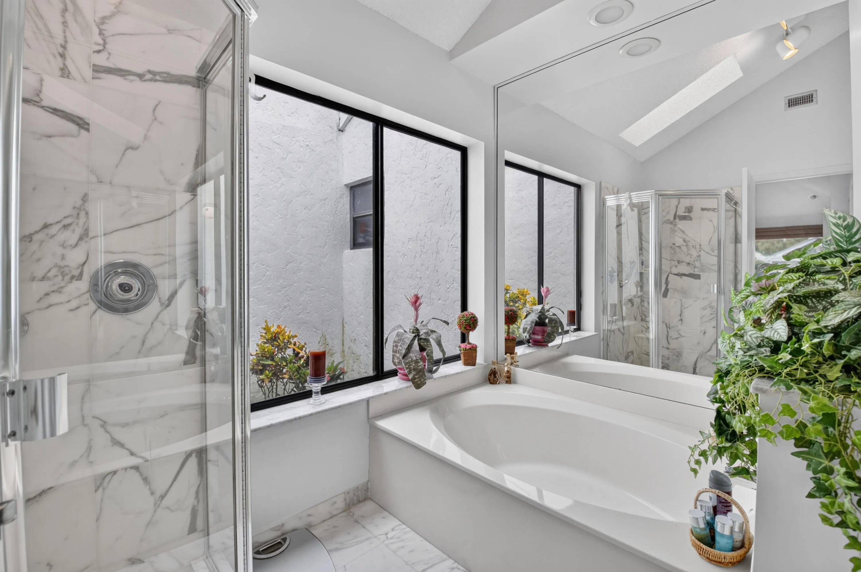 Recessed tub with an expansive mirror, enclosed shower with marble-look tile, and a vaulted ceiling with a skylight
