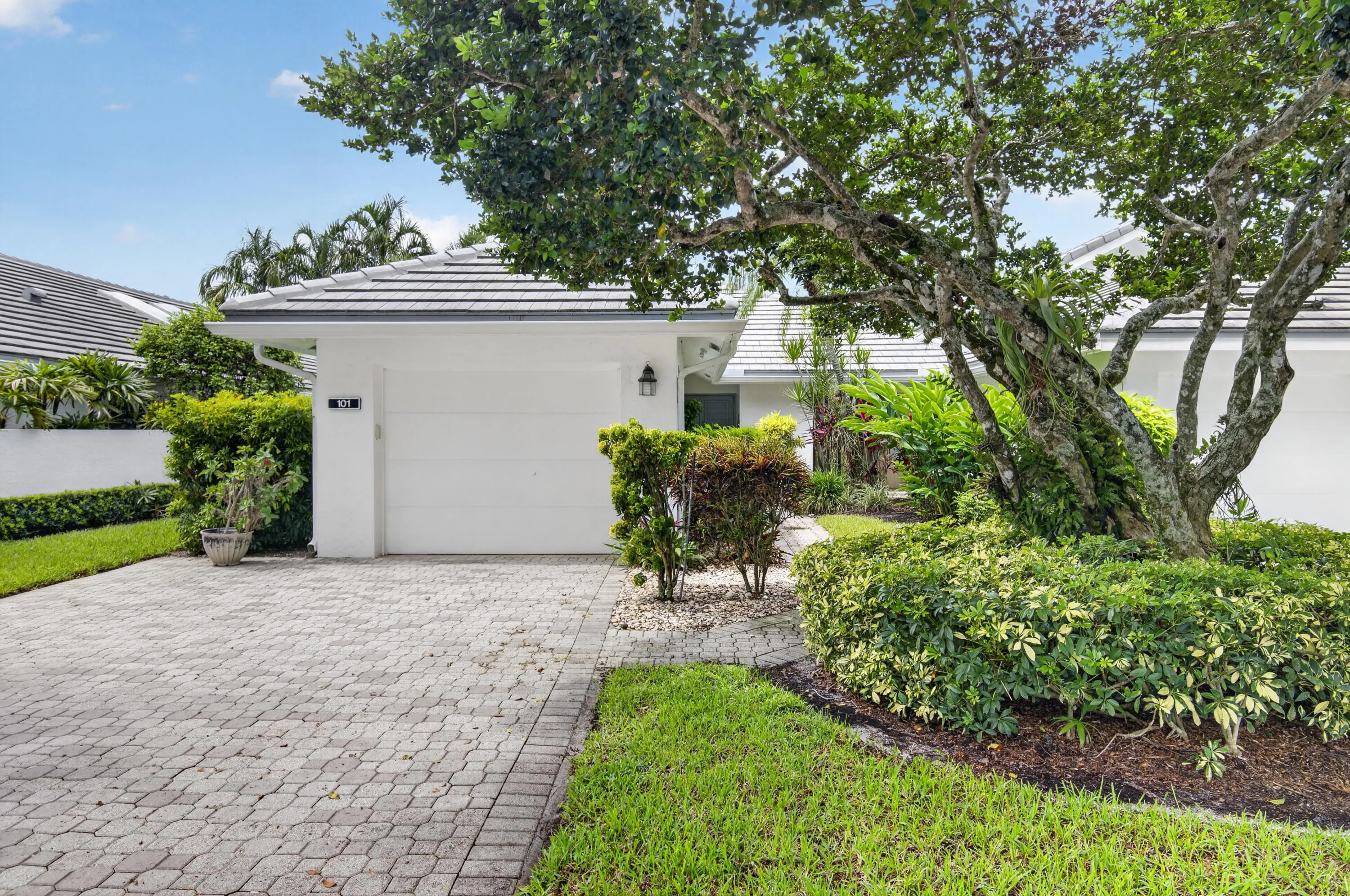 White exterior with a tiled roof, paver driveway, and an attached garage