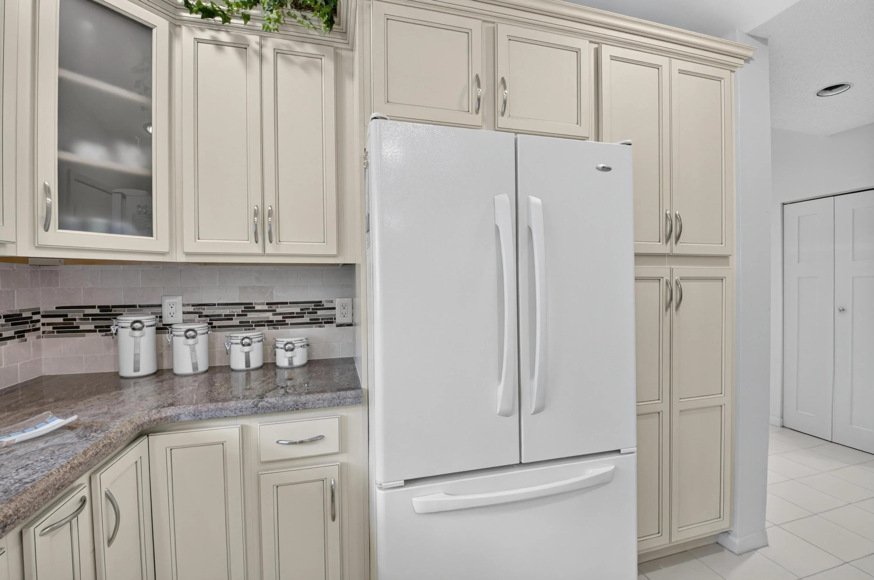 Full-height cabinetry, glass-front upper cabinet, stone countertop, tile backsplash, and built-in refrigerator