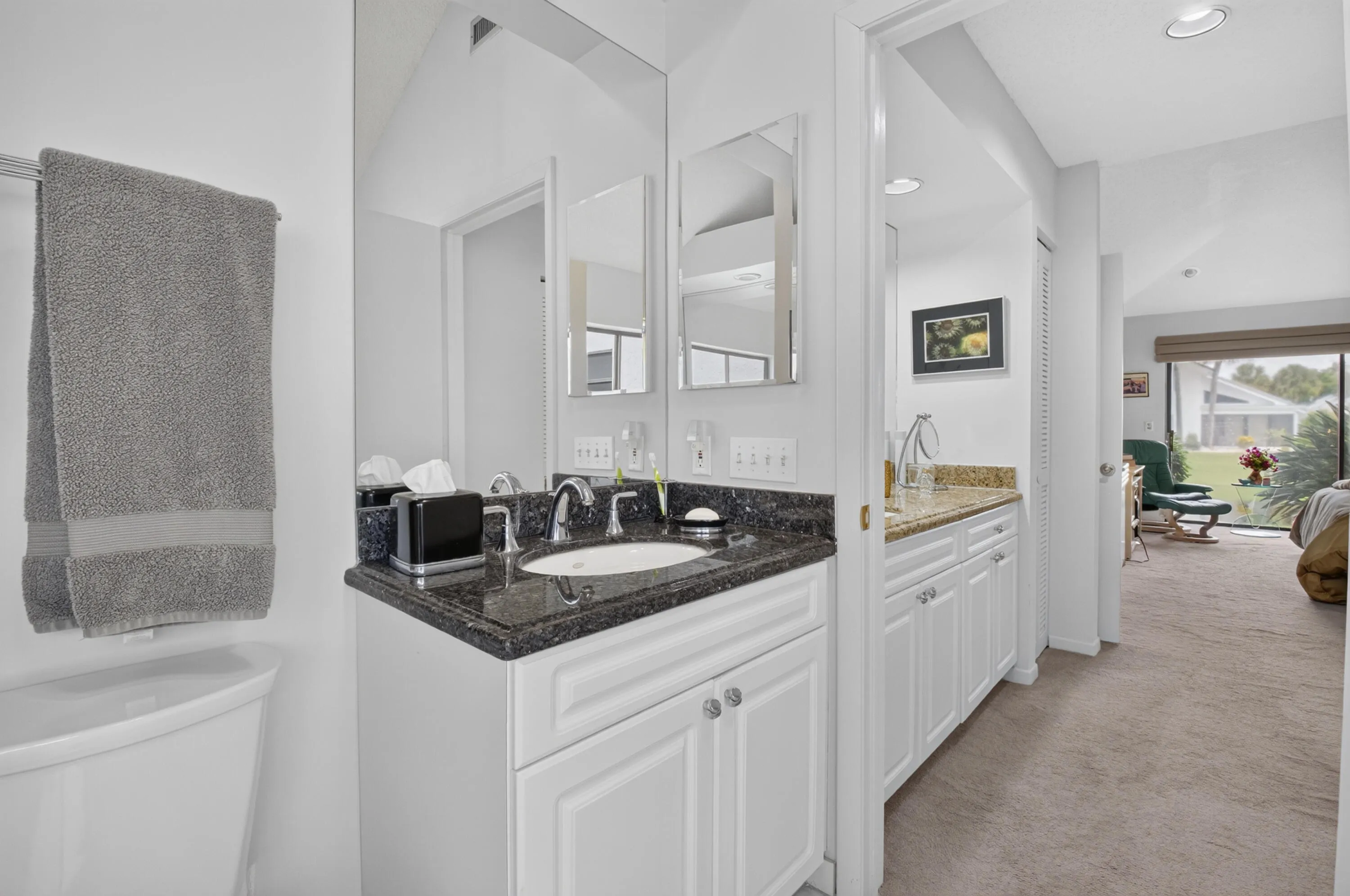 Vanity with dark countertop, white cabinetry, undermount sink, and polished chrome fixtures
