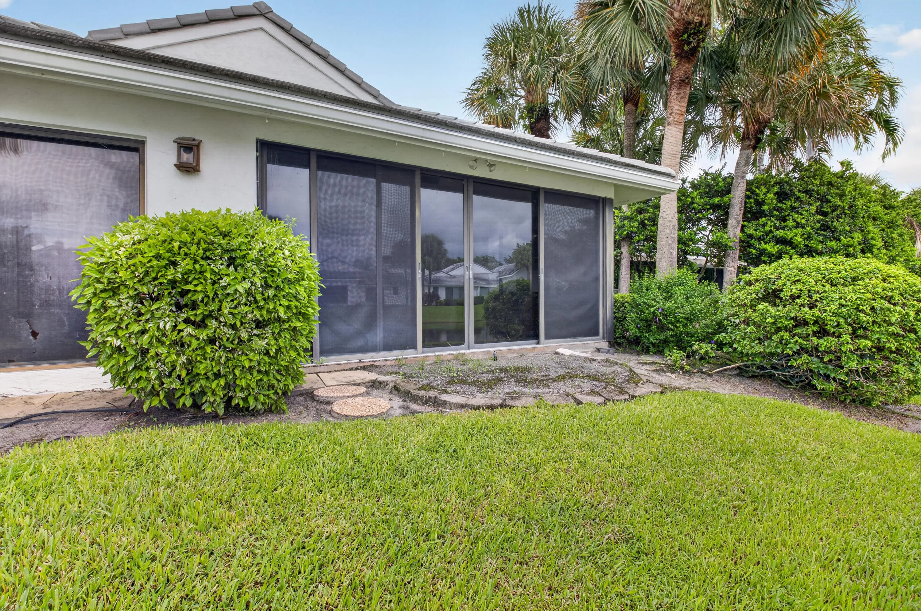 Modern residence showcasing expansive manicured lawn, mature palm trees, and professionally landscaped foundation plantings