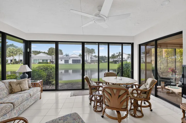 Screened lanai featuring expansive glass panels, white tile flooring, and a ceiling fan