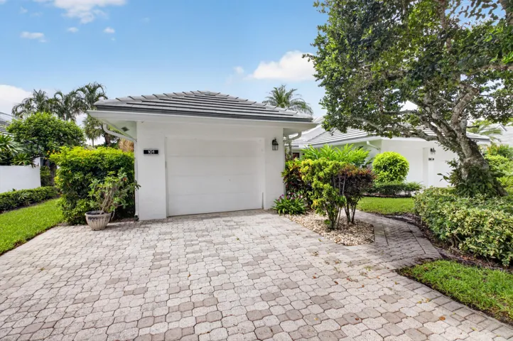 Paver driveway and walkway, lush landscaping, white exterior, garage with white door, gray tile roof