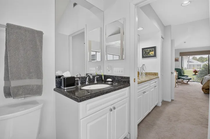 Vanity with dark countertop, white cabinetry, undermount sink, and polished chrome fixtures