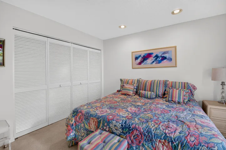 Bright secondary bedroom featuring carpeted flooring, louvered closet doors with multiple panels, recessed ceiling lighting, and coordinating striped bedding