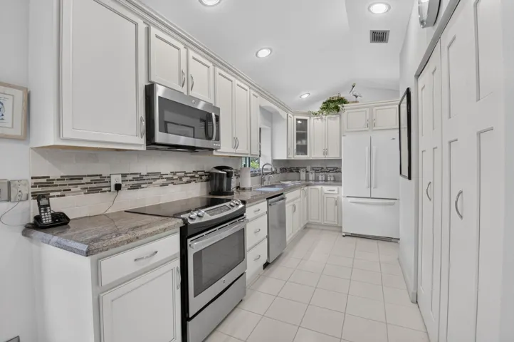 Vaulted ceiling kitchen featuring white cabinetry, tile flooring, stone countertops, stainless steel microwave, and integrated panel pantry storage