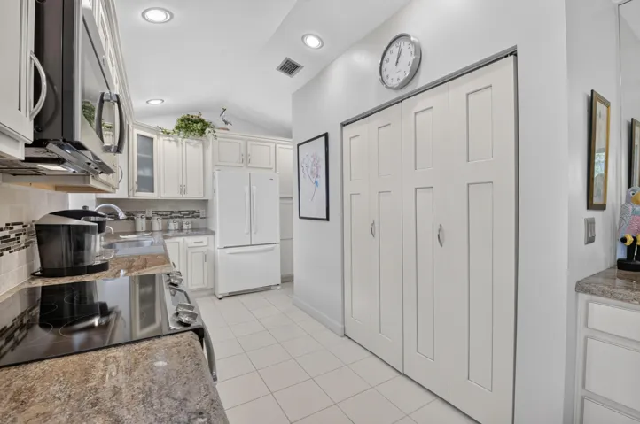 Vaulted ceiling, recessed lighting, white cabinetry, tile flooring, and a patterned backsplash