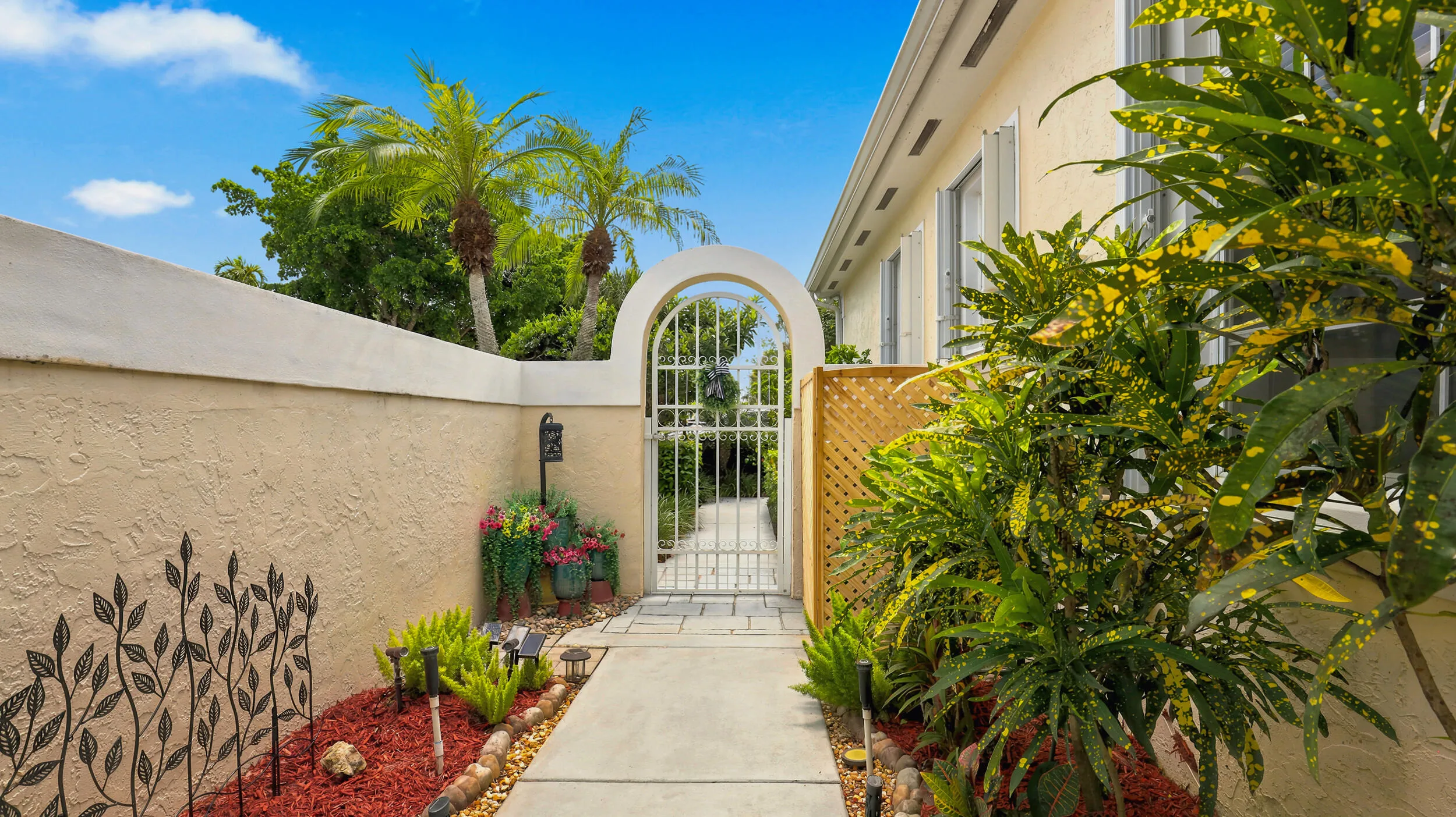 Charming private walkway framed by lush tropical landscaping leading toward the gated entrance.