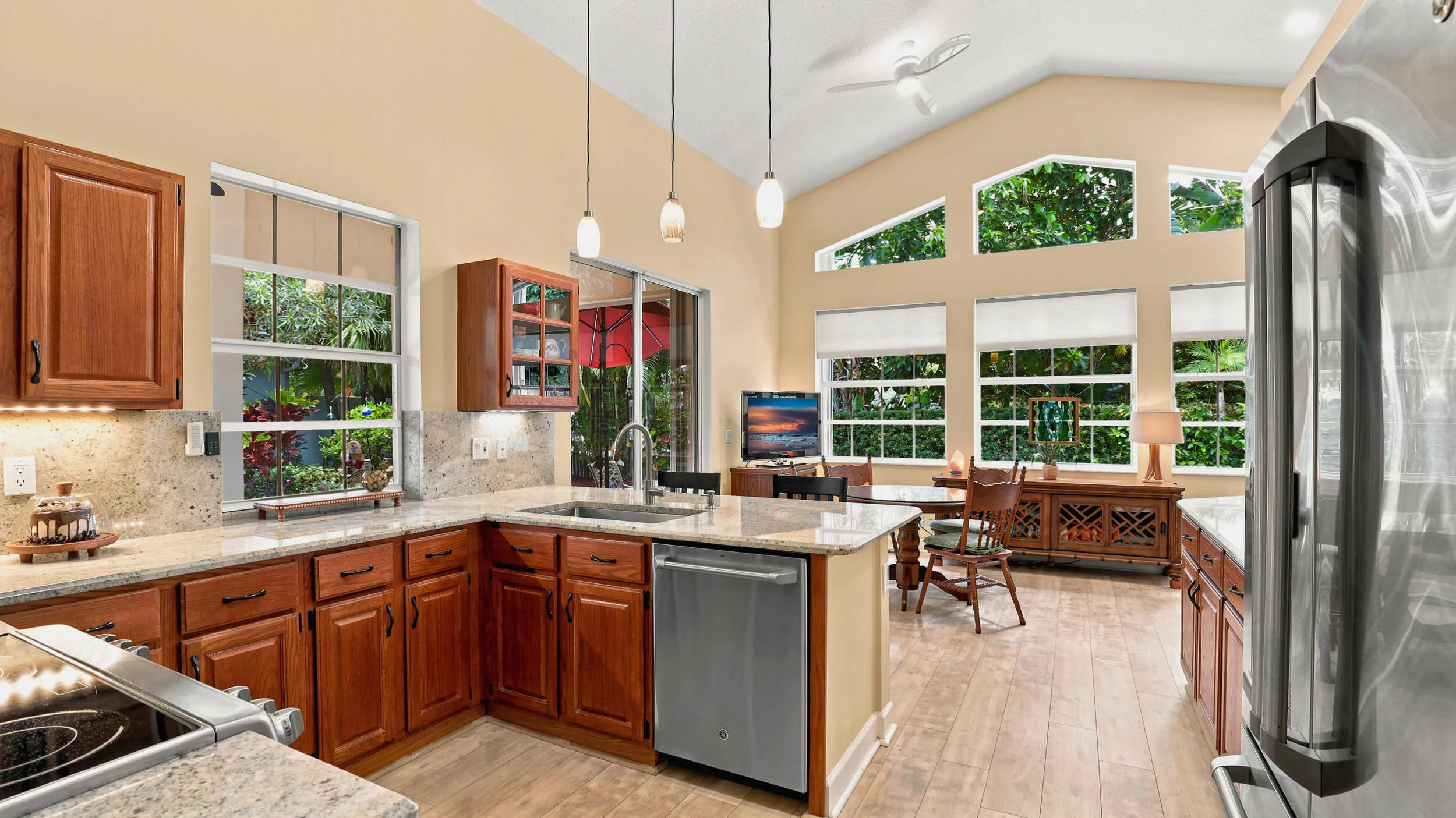 Bright kitchen opening to a casual dining area surrounded by large windows and natural light.