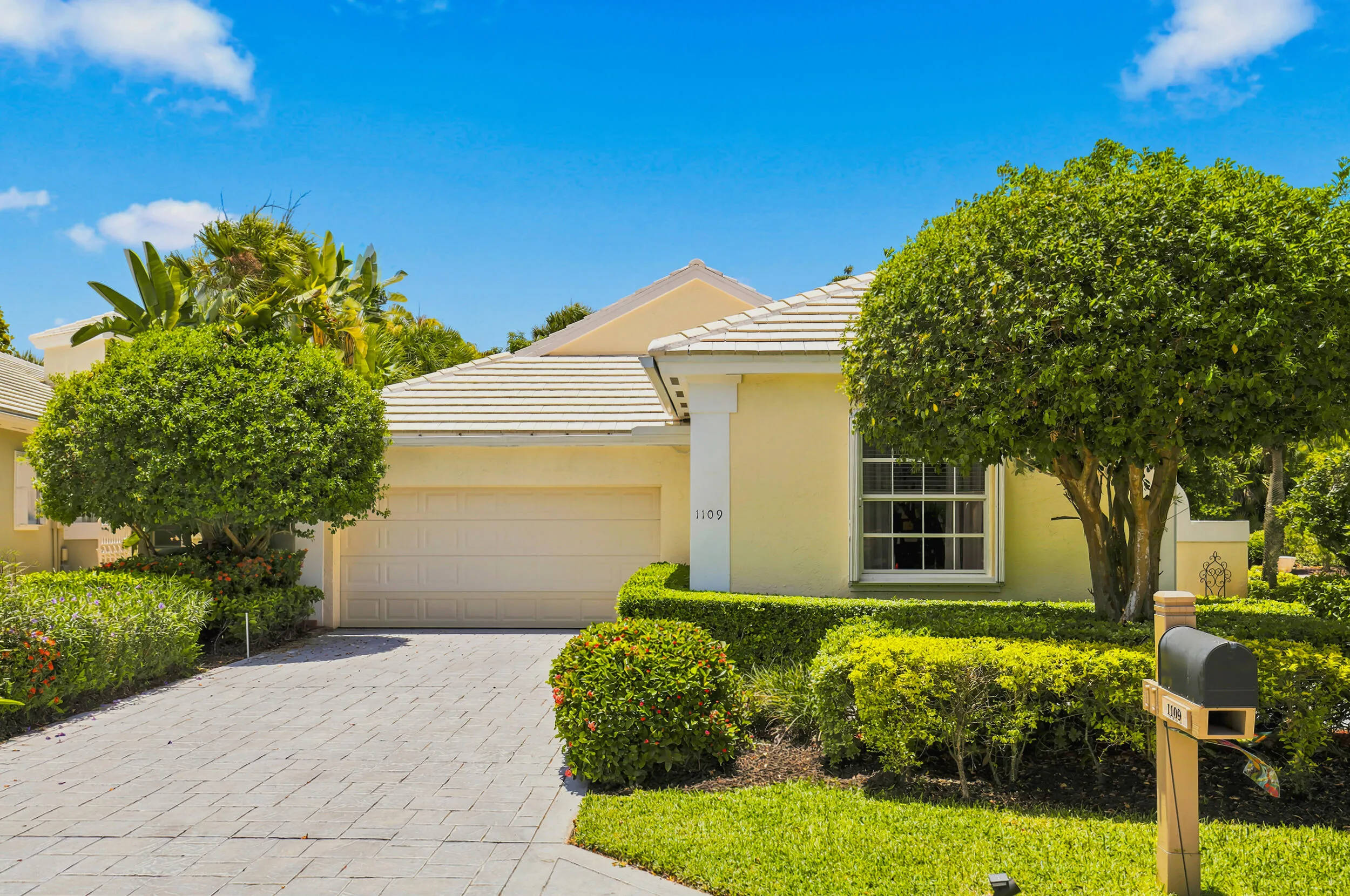 Welcoming single-story exterior with an attached garage, paver driveway, and beautifully maintained landscaping.