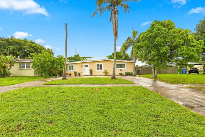 Wide front view showcasing the home, spacious lawn, mature trees, and driveway.
