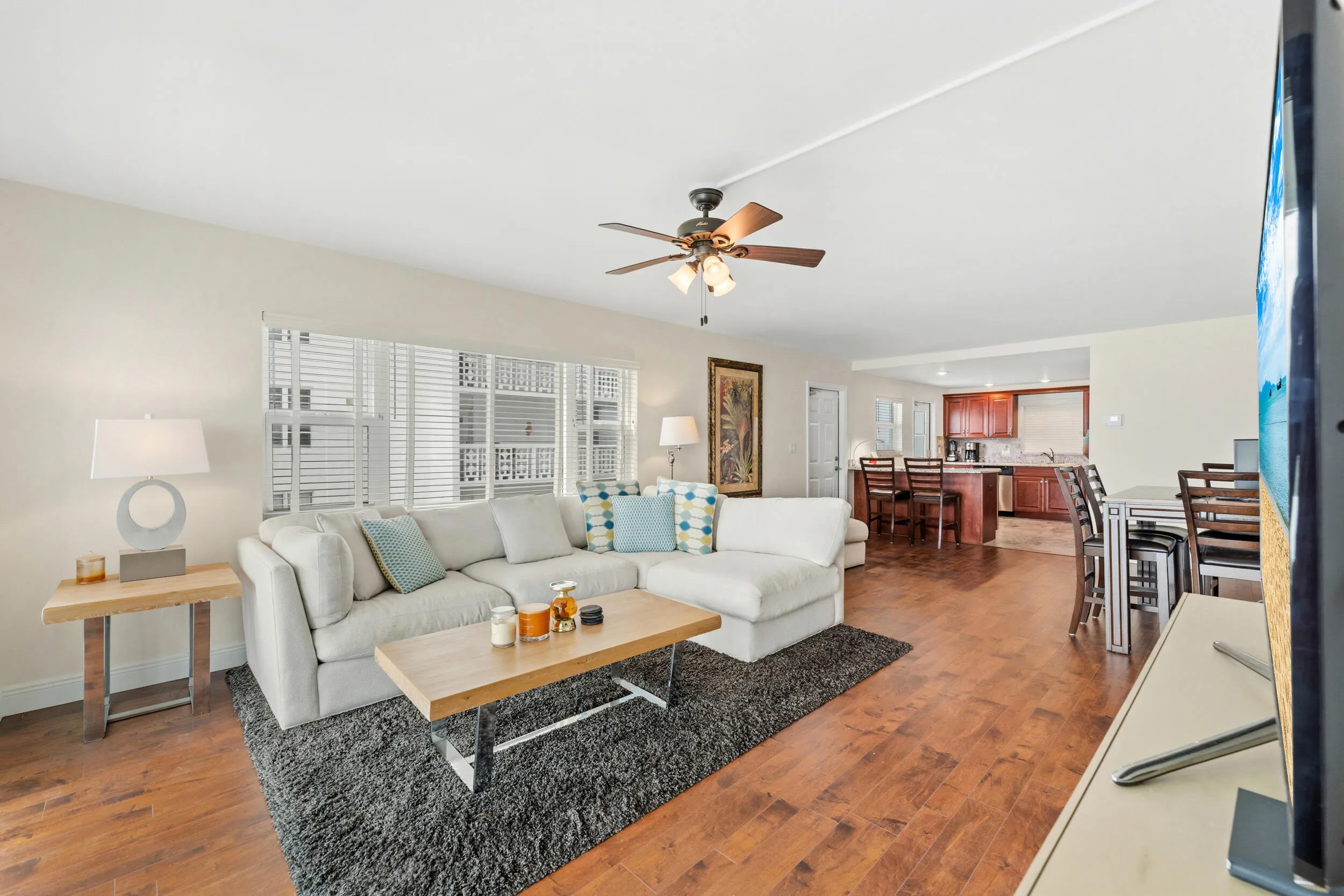 Open-concept living area with wood-finish flooring, a ceiling fan with integrated lighting, and white horizontal window blinds