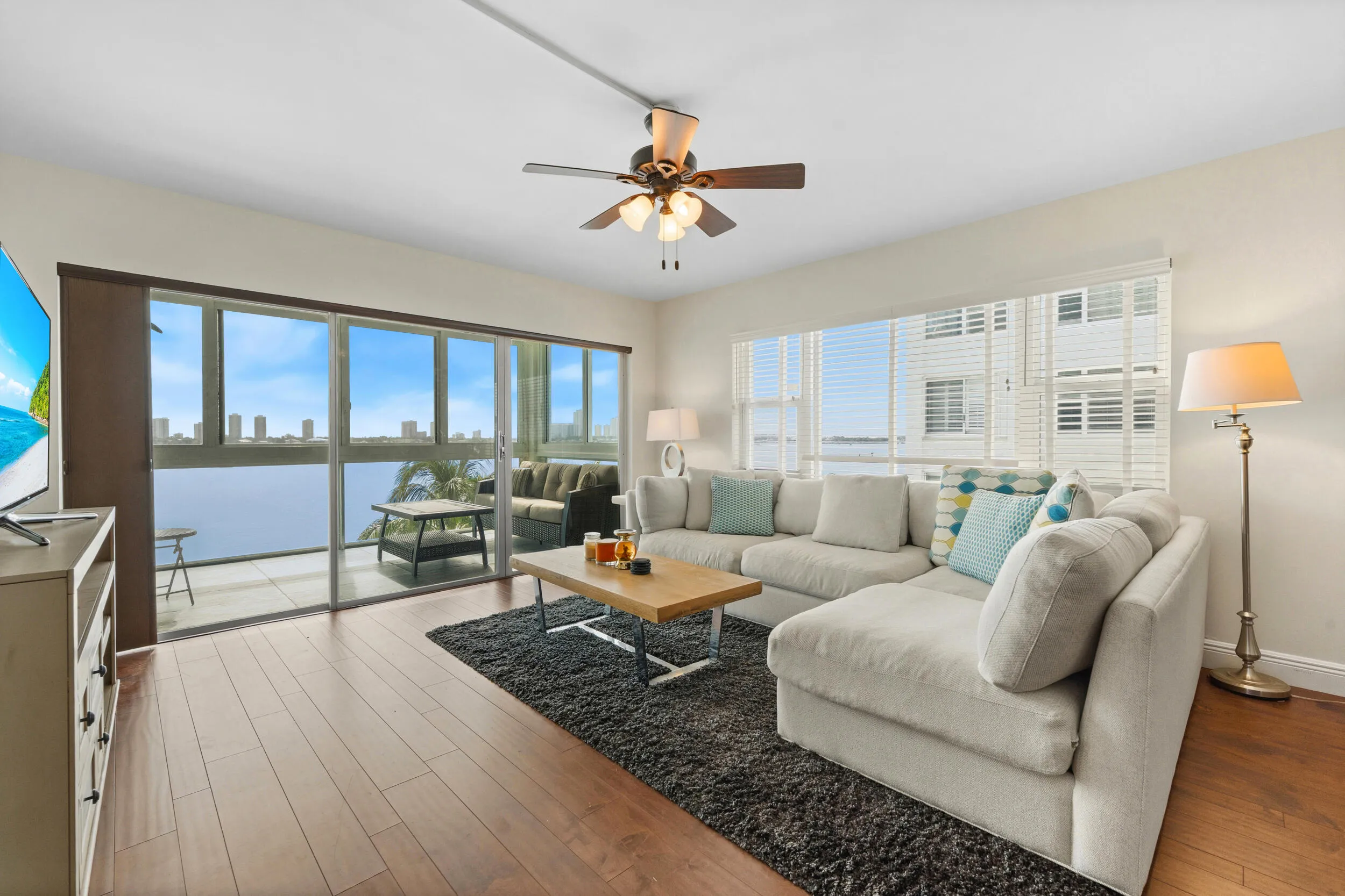 Wood-finish flooring, ceiling fan with integrated lighting, expansive sliding glass doors, white horizontal blinds, and a built-in wall unit