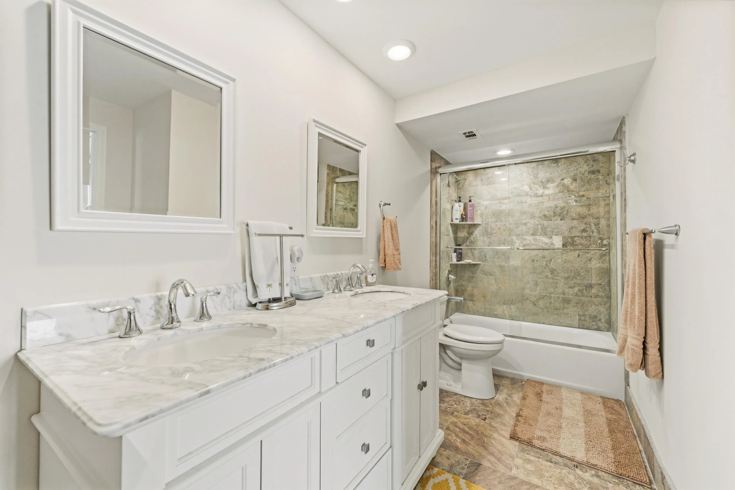 Dual vanity with a stone countertop and undermount sinks, chrome fixtures, framed mirrors, a tiled shower with a sliding glass door, and a built-in bathtub
