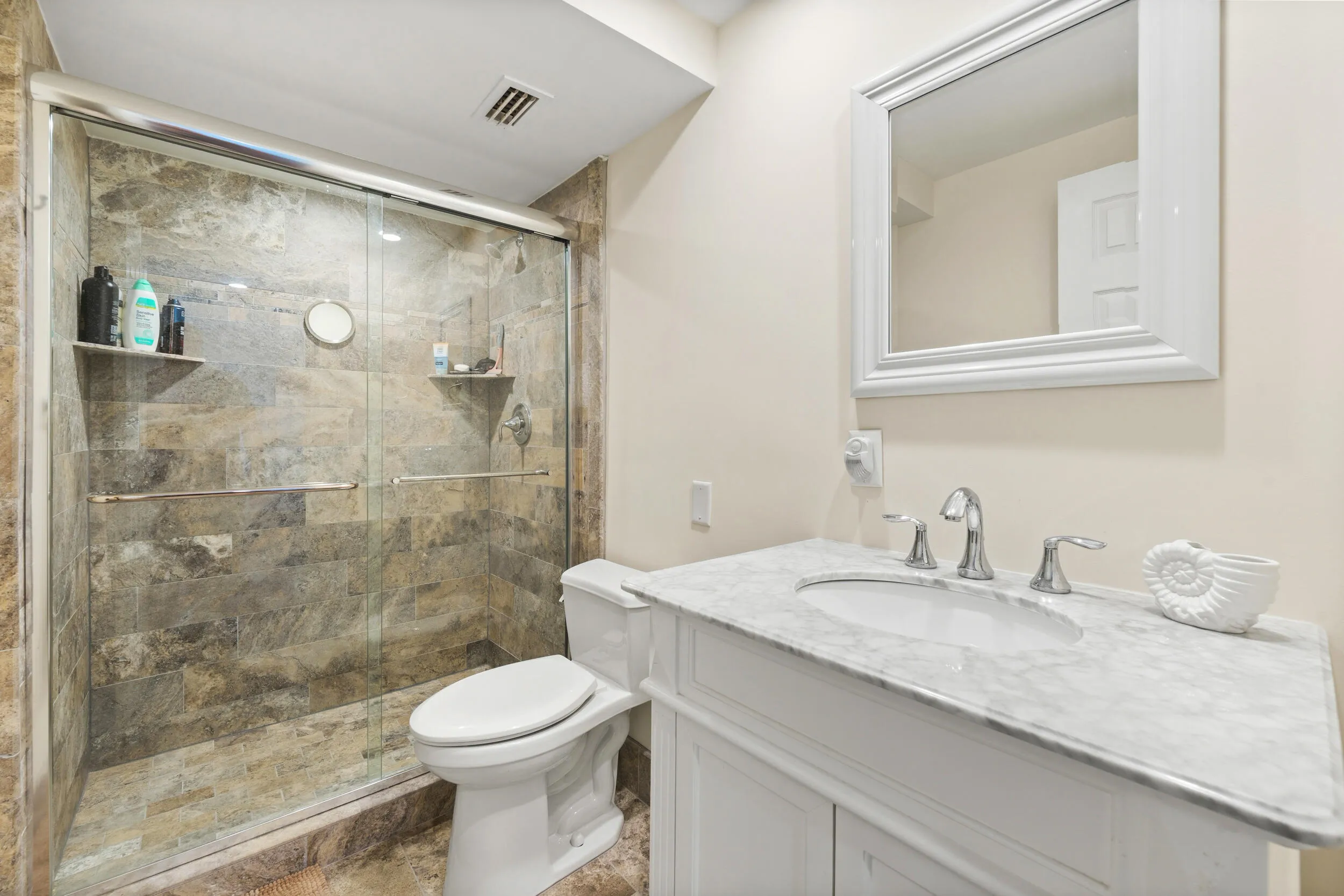 Walk-in shower with tiled walls and glass enclosure, white vanity with stone countertop, undermount sink, and chrome fixtures