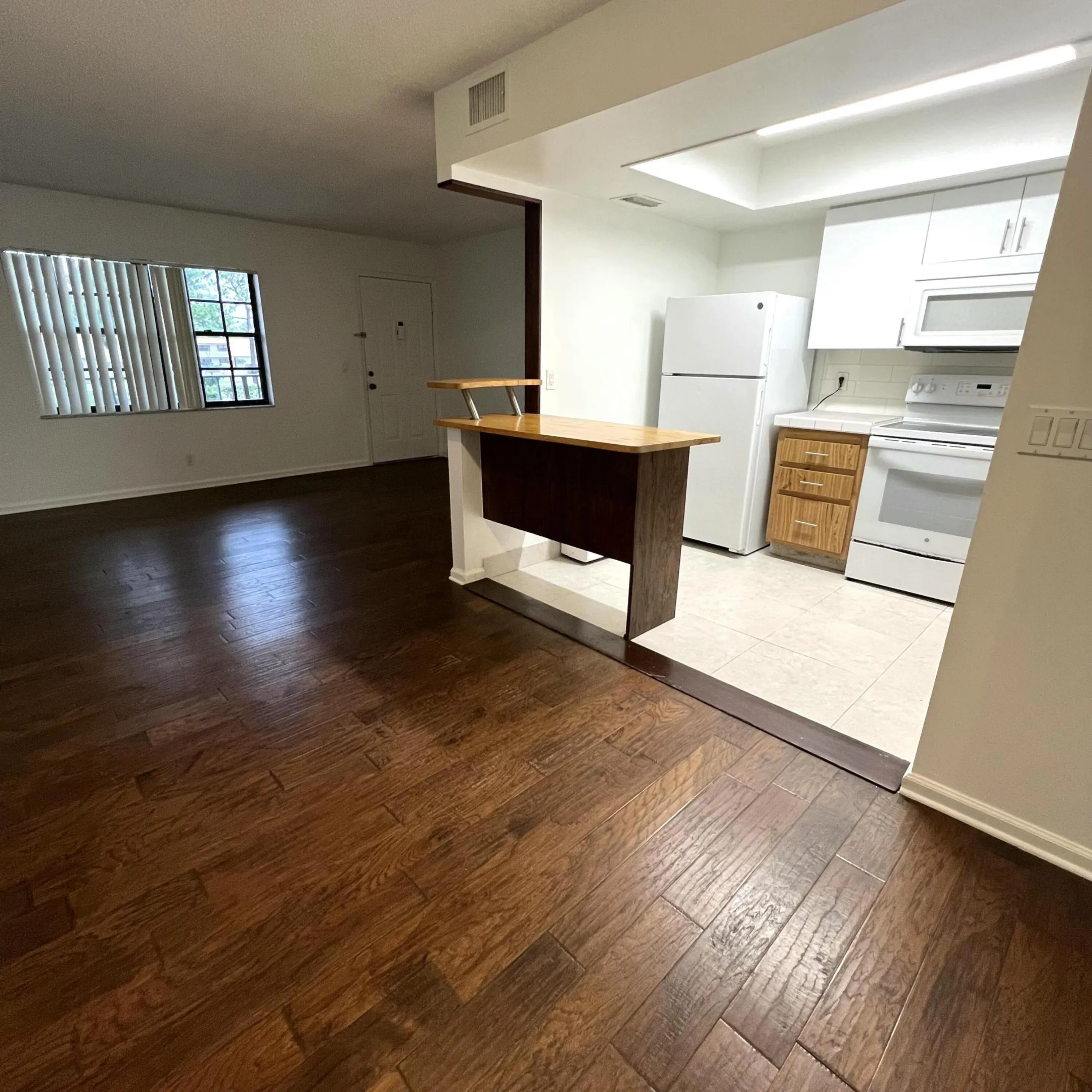 Wood-finish flooring, white kitchen cabinetry, white appliances, and a built-in breakfast bar