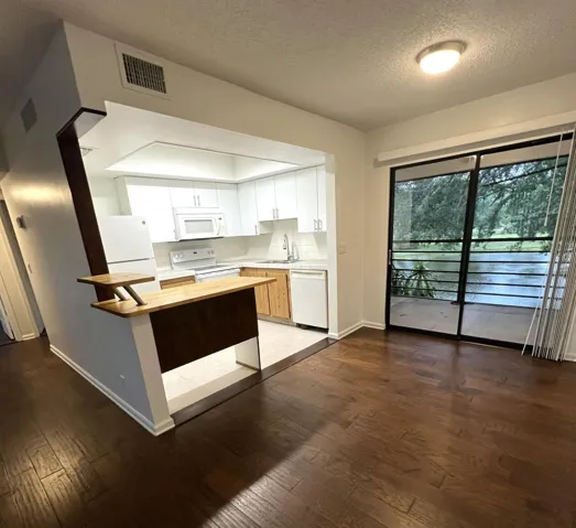 Open-concept living area featuring wood-finish flooring, a kitchen with white cabinetry and appliances, a built-in breakfast bar, and sliding glass doors opening to an outdoor space