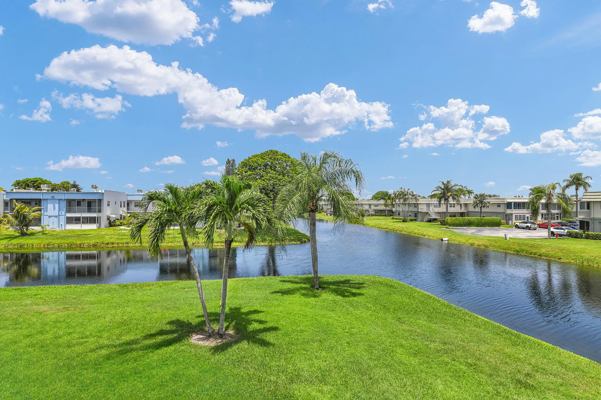 Expansive canal-front property featuring lush green lawns, mature palm trees, and clear blue water