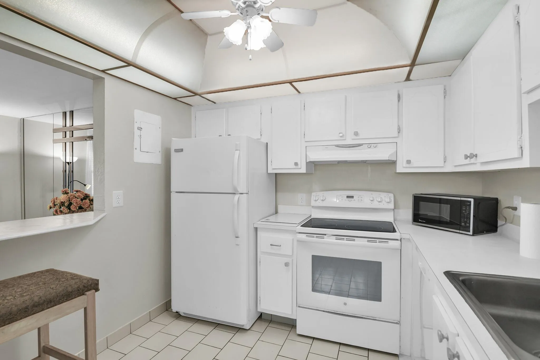 Kitchen featuring white cabinetry, white appliances, tile flooring, a breakfast bar, and a drop ceiling with integrated lighting
