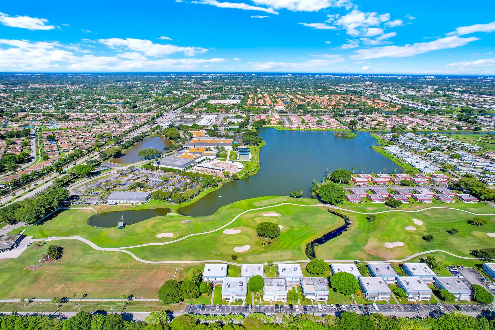 Expansive aerial view showcasing a large body of water, extensive golf course greens, and numerous residential structures