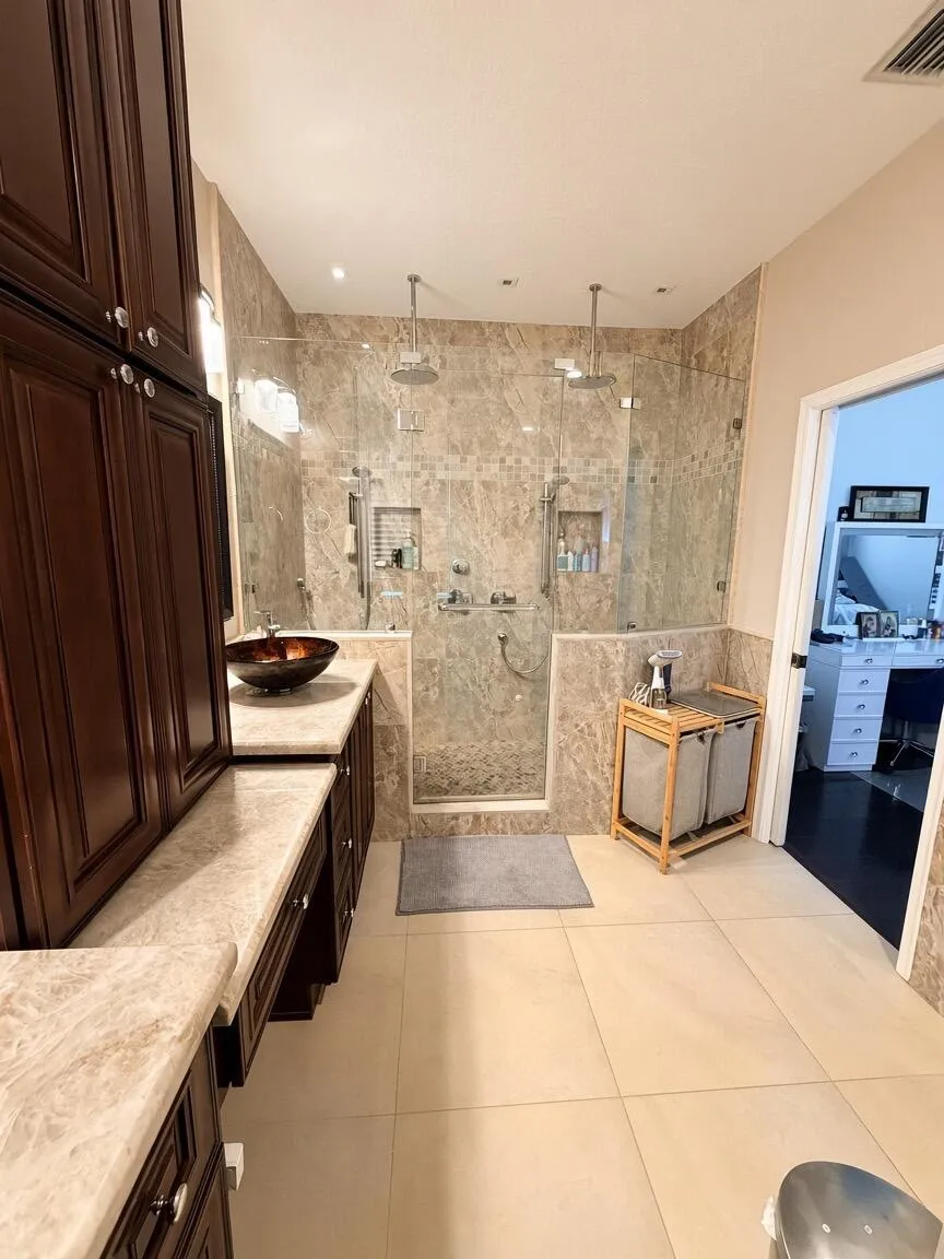Dual rain shower heads, floor-to-ceiling glass shower enclosure, built-in shower niches, extensive dark wood-finish cabinetry, and light-toned tile flooring
