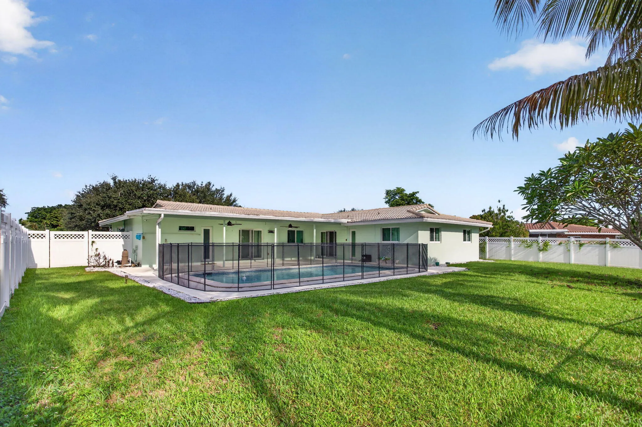 Expansive green lawn, fenced perimeter, in-ground swimming pool with safety barrier, and a single-story residence with a patio