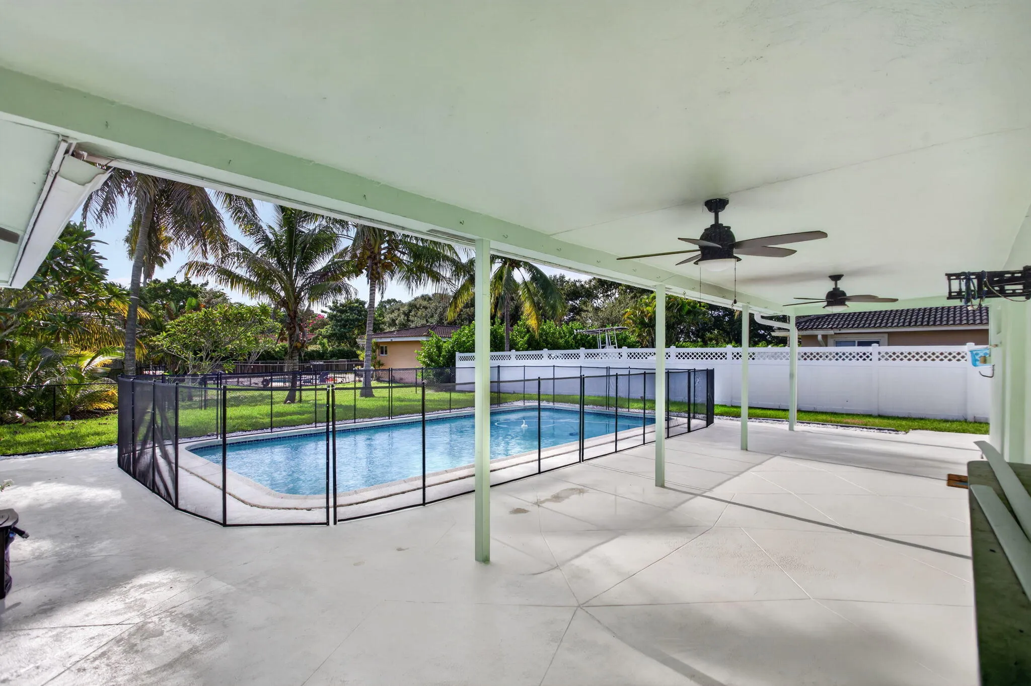Covered patio with integrated ceiling fans, expansive concrete decking, and a fenced swimming pool
