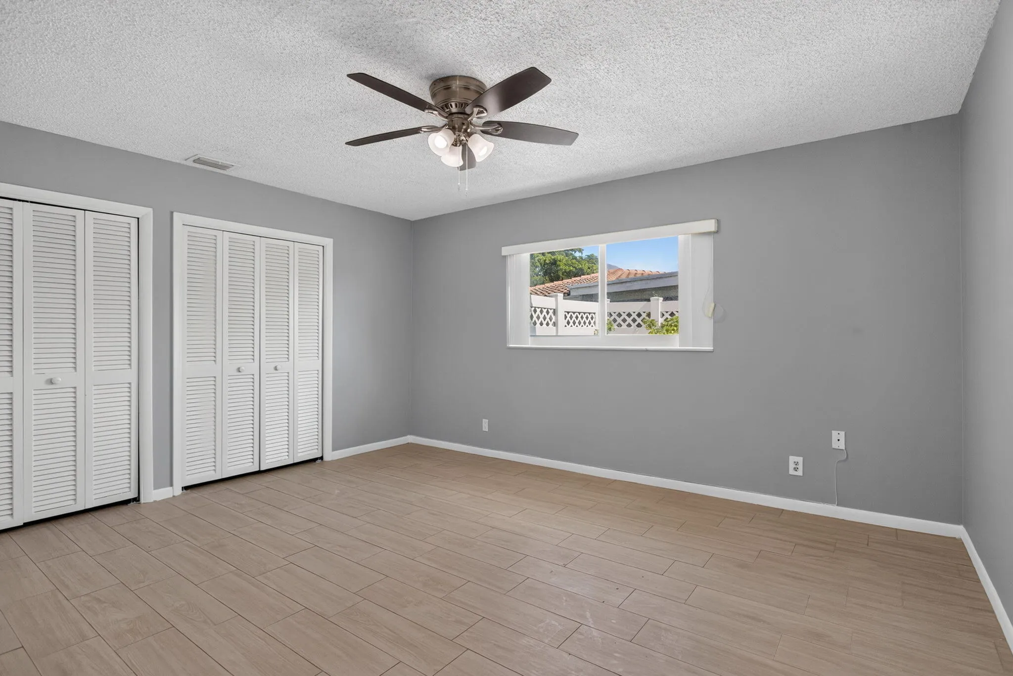 Wood-finish flooring, louvered bi-fold closet doors, ceiling fan with integrated lighting, and a single window