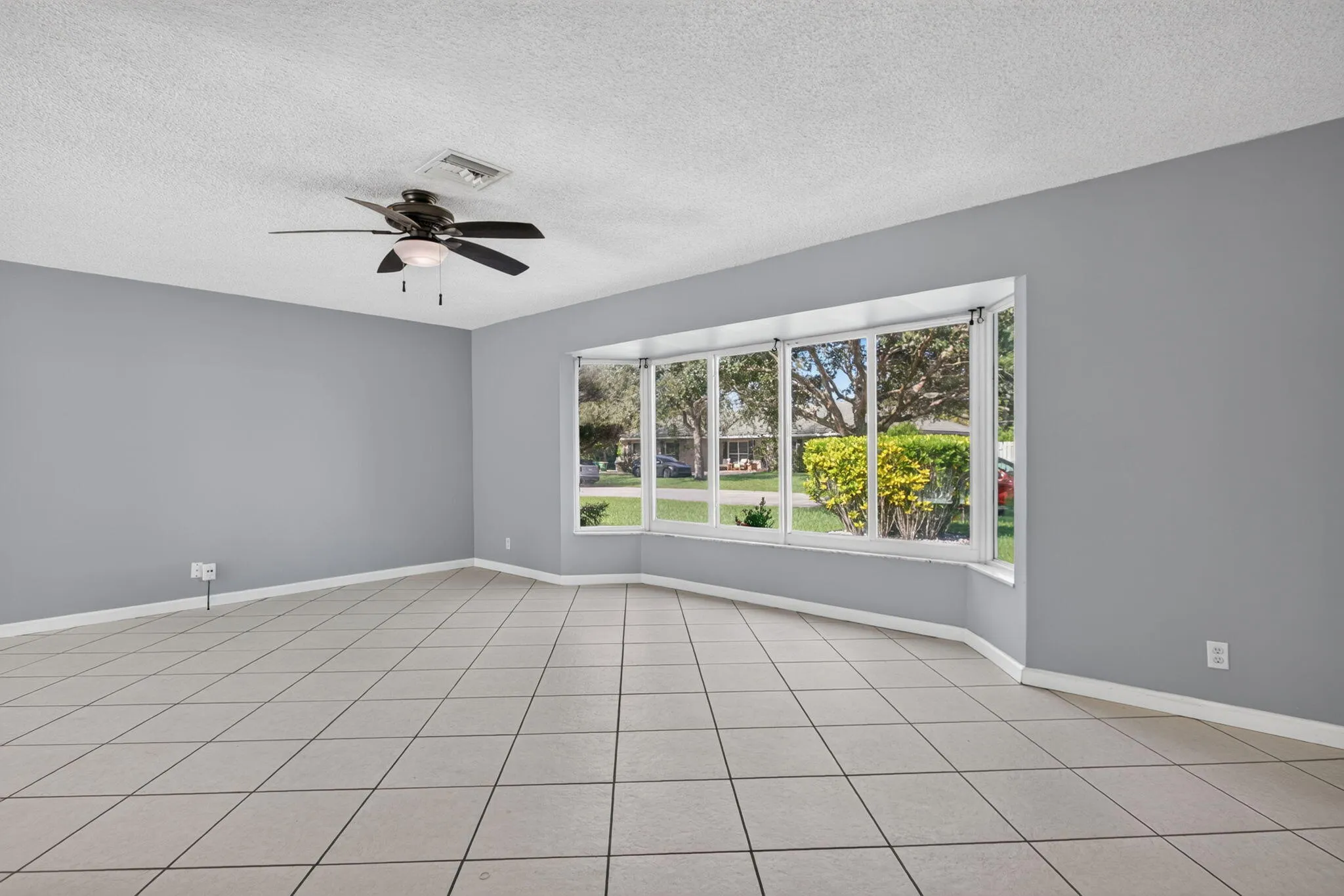 Spacious room featuring neutral tone tile flooring, a multi-pane bay window, and a ceiling fan with integrated lighting