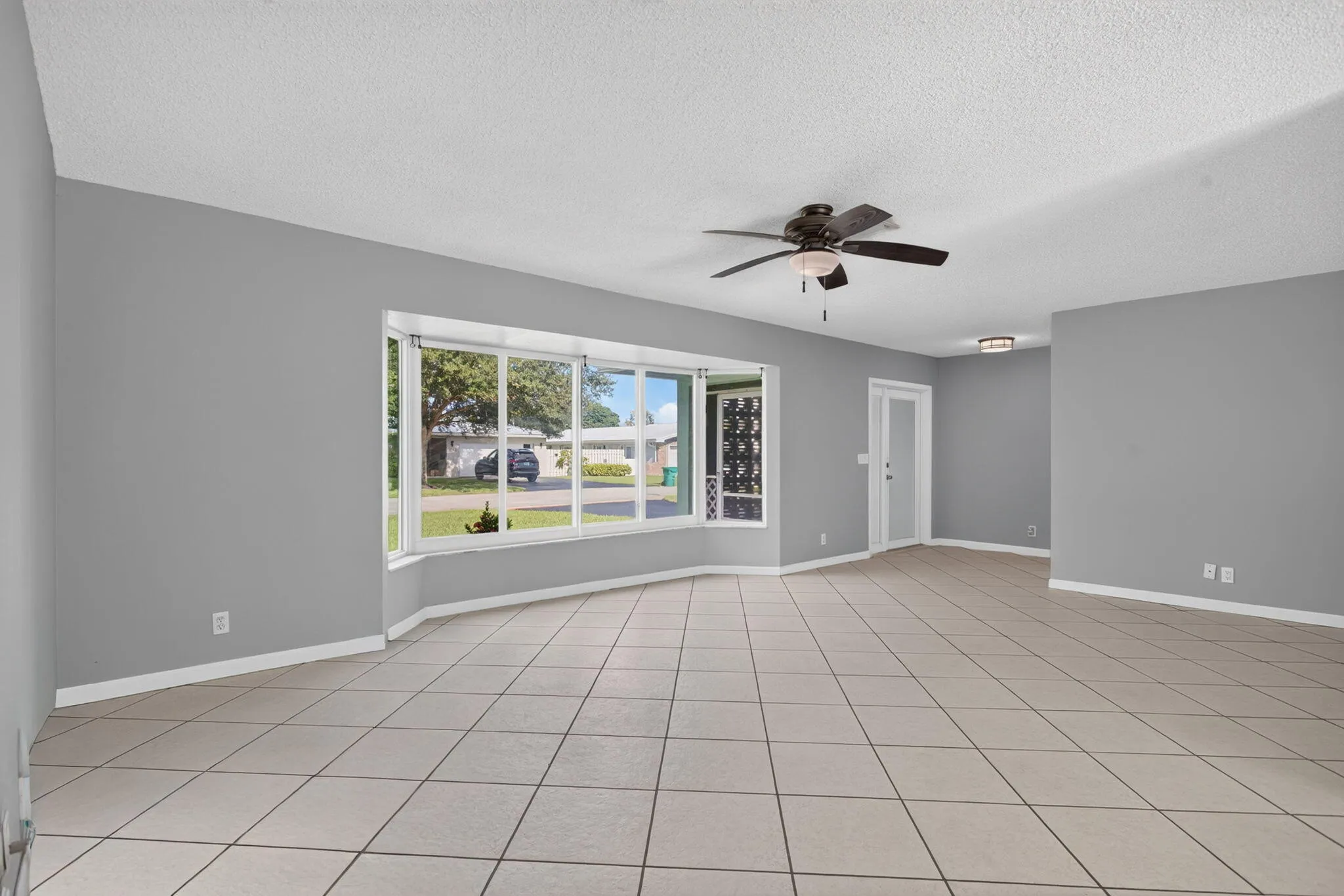 Expansive room featuring tile flooring, a bay window, ceiling fan, and a flush-mount ceiling light