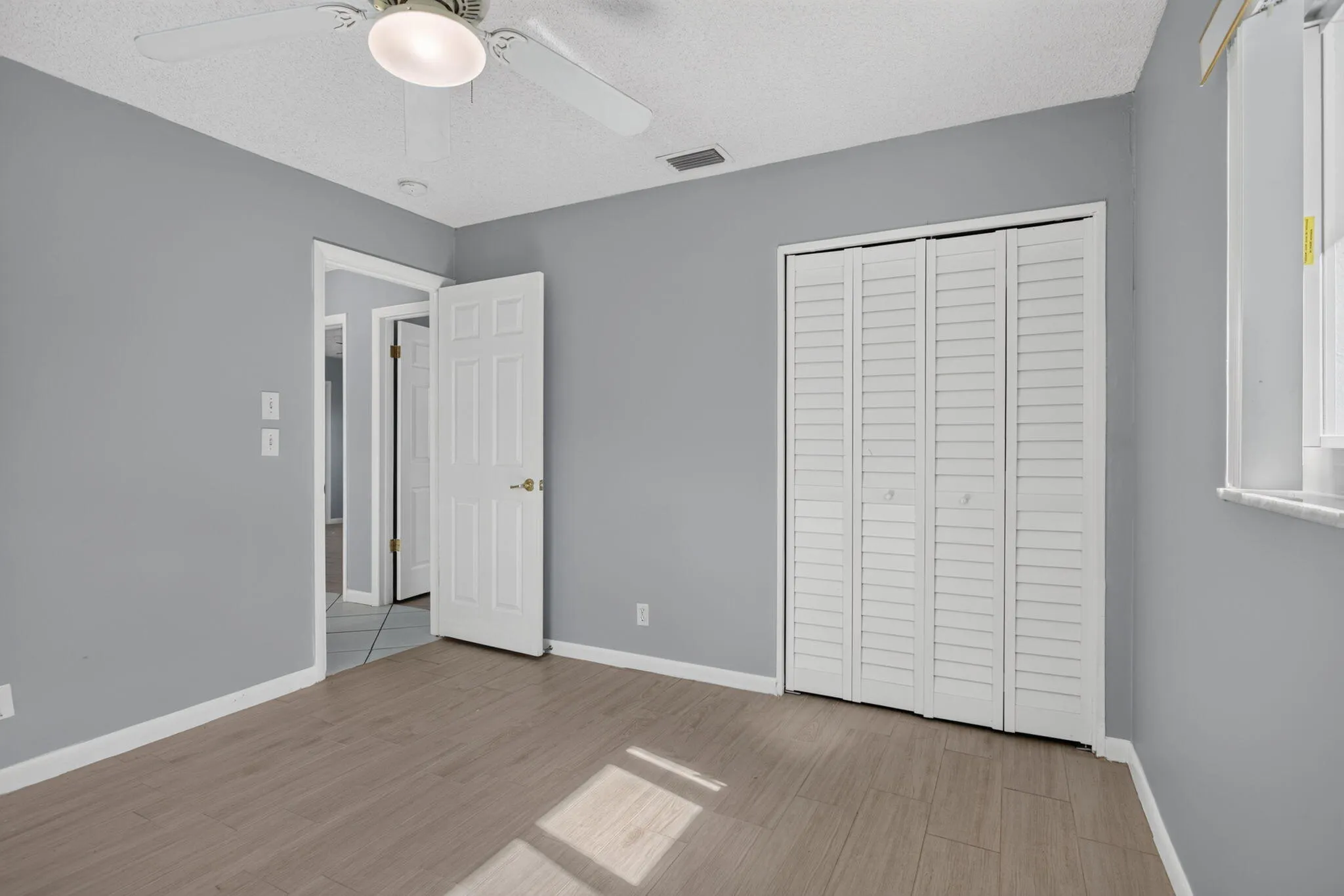 Wood-finish flooring, ceiling fan with integrated lighting, louvered bi-fold closet doors, and light gray wall finish
