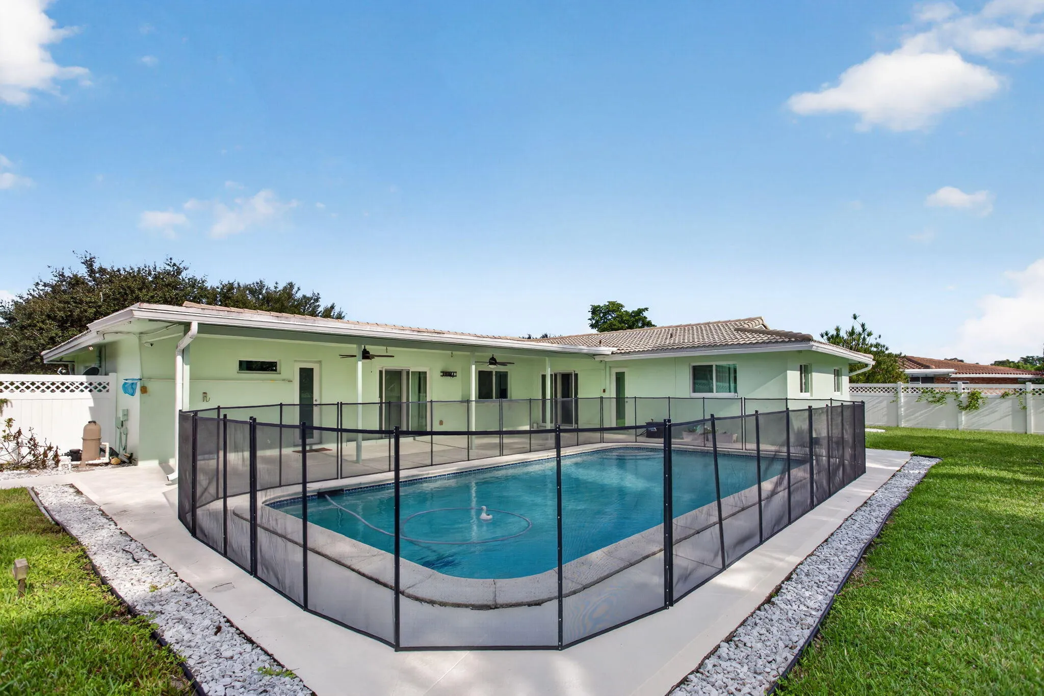 Outdoor pool with safety fencing, concrete patio, expansive green lawn, and gravel landscaping